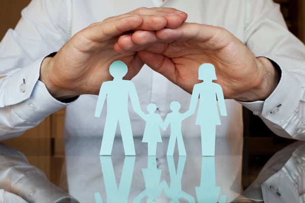 Cupped hands held above a paper cutout of a family of four on a glossy table