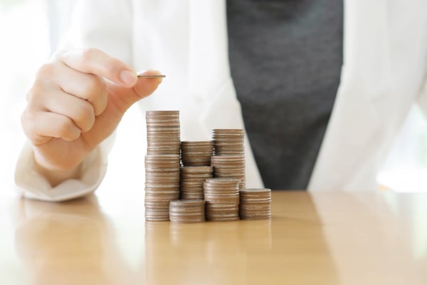Hand placing a coin on top of stacks of coins on a wooden table