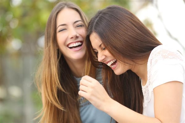 A person leans in to speak closely with another while the two sit together outdoors.