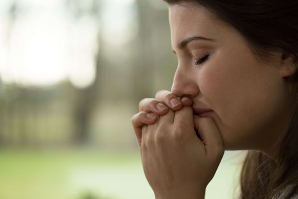 Close-up of a woman in profile with eyes closed and hands pressed to her mouth, appearing distressed