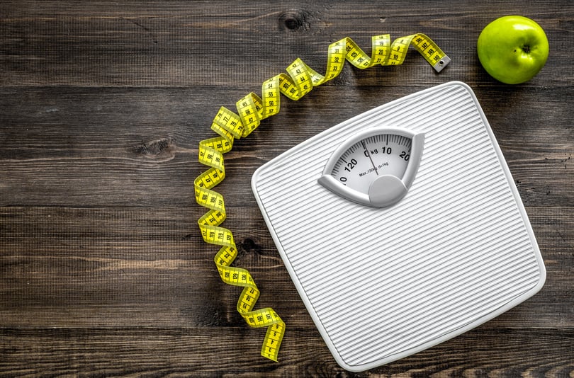 Bathroom scale, a yellow measuring tape and a green apple on a dark wooden surface