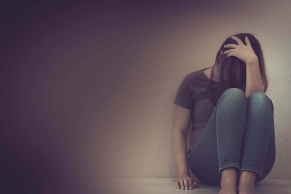Woman sitting on the floor against a wall with her knees drawn up and her head in her hand