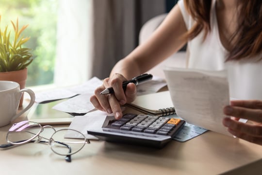 Woman holding a pen over a calculator while reviewing receipts and bills at a desk