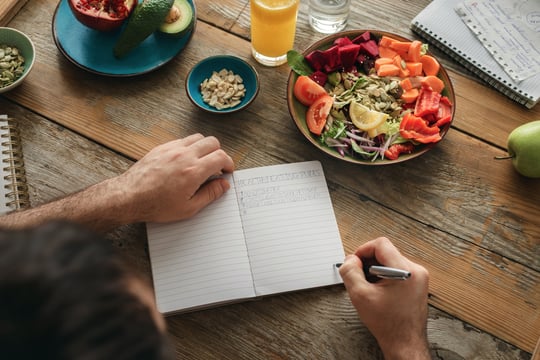 Person writing a Healthy Eating Rules list in a notebook beside a bowl of colorful salad