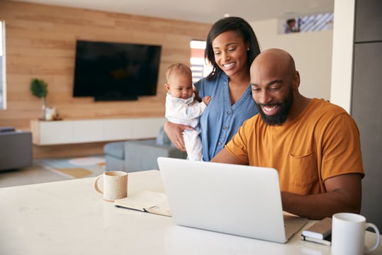 Smiling couple with a baby looks at a laptop on the kitchen counter at home