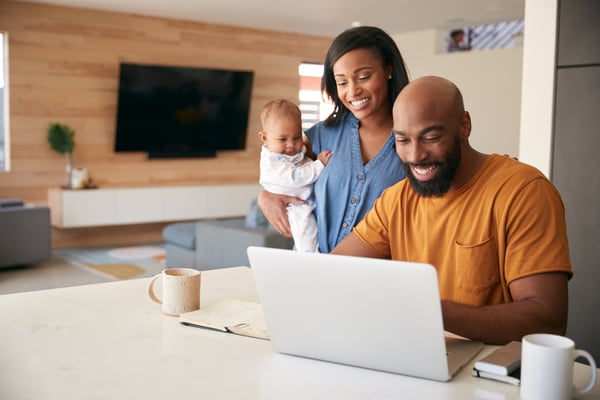 Smiling couple with a baby looks at a laptop on the kitchen counter at home