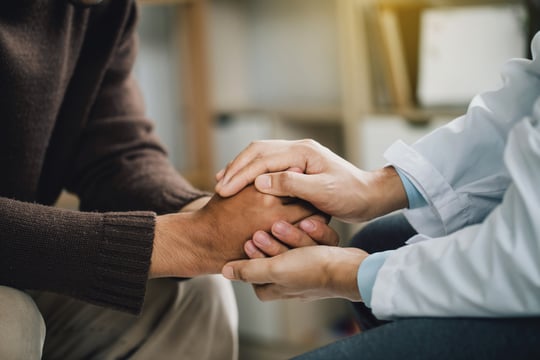 Close-up of a person in a white coat holding another person's hands in comfort
