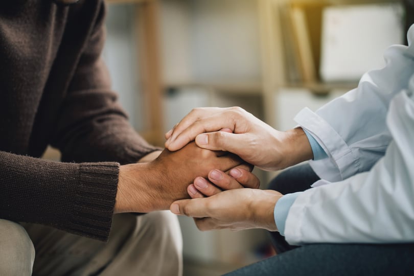Close-up of a person in a white coat holding another person's hands in comfort