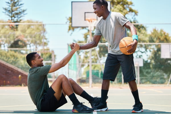 someone helping someone up, after falling on the basketball court