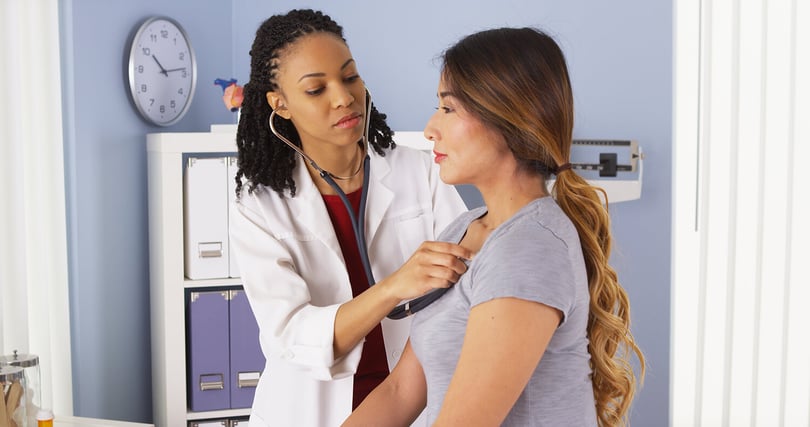 Doctor listens to a patient's heartbeat with a stethoscope in an exam room