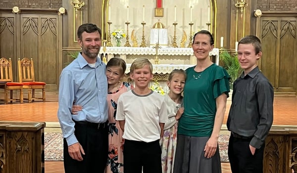 Smiling family of six, two adults and four children, standing in front of an ornate church altar
