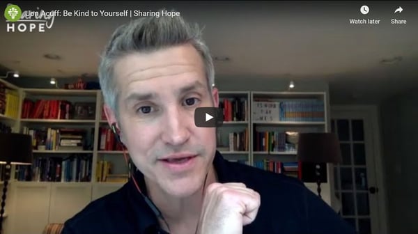 Jon Acuff speaking in front of bookshelves in a still from the Sharing Hope video Be Kind to Yourself