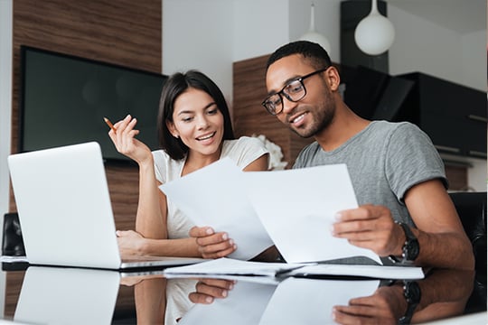 Smiling man and woman reviewing papers together at a laptop in a modern home