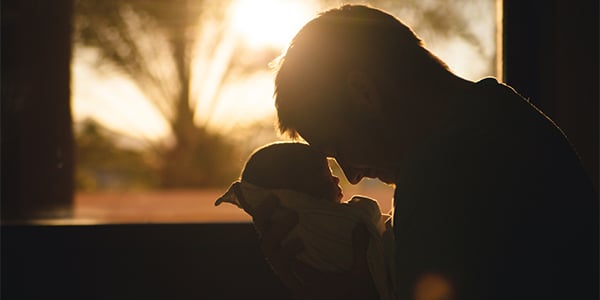 Silhouette of a man cradling a newborn close to his face in front of a sunlit window
