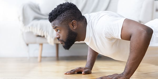 Man in a white T-shirt doing push-ups on a living room floor