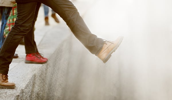Close-up of a person in tan boots stepping off a high stone curb