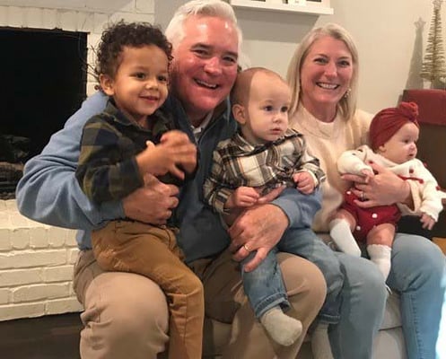 Britt and Julie Todd smiling at home with three young children on their laps
