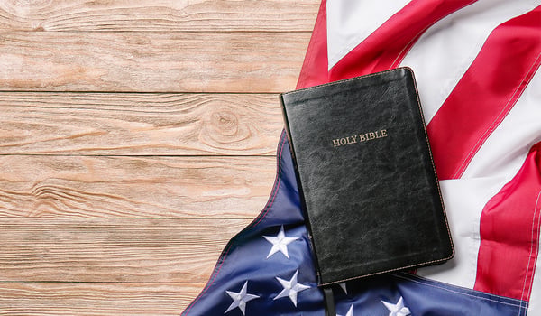 A bible and an American flag laying flat on a wood table.