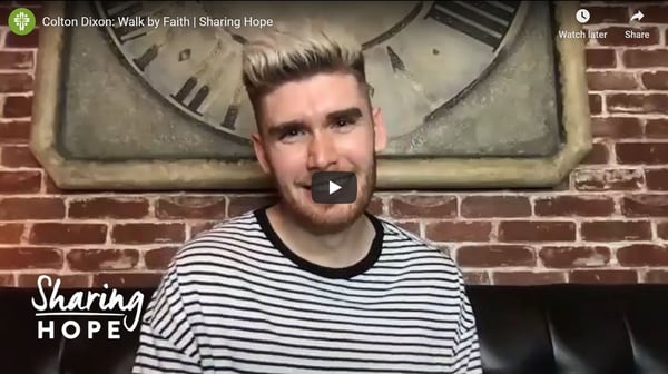 Colton Dixon in a striped shirt before a brick wall in a still from the Sharing Hope video Walk by Faith