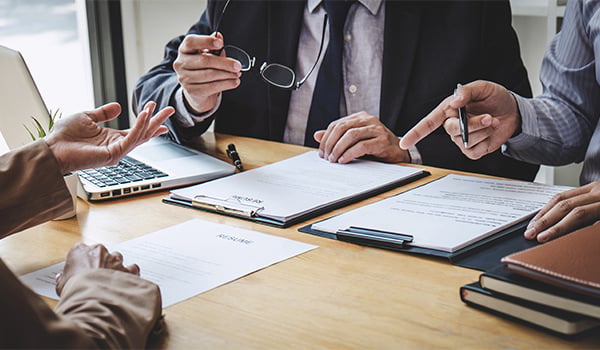 People in business attire reviewing documents on clipboards around a meeting table