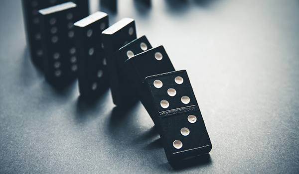 A curved line of black dominoes with white dots toppling one after another