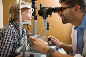 Eye doctor examining a smiling young child's eyes with a slit lamp