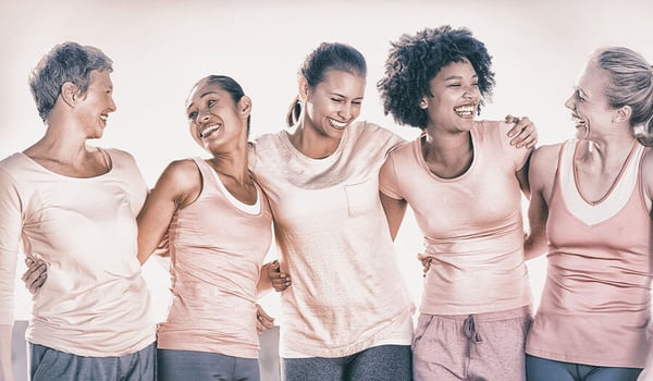 Five women of different ages in pink tops laughing together arm in arm