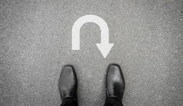 Person in black dress shoes stands on asphalt facing a white painted U-turn arrow