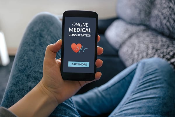 Person on a couch holding a smartphone that displays an online medical consultation screen