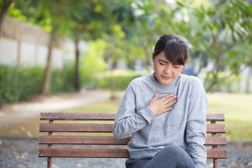 Woman sitting on a park bench with a hand pressed to her chest in discomfort