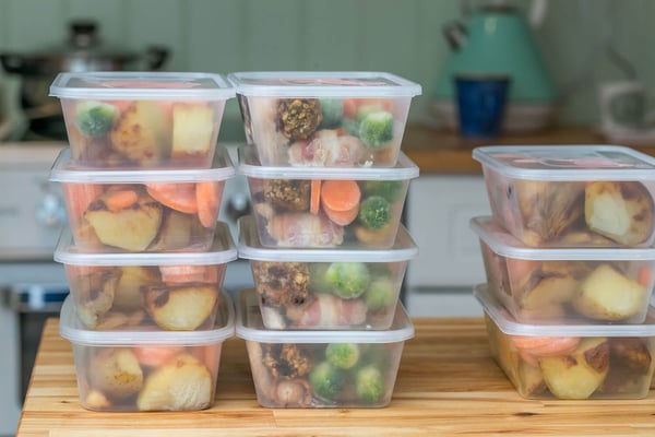 Stacked meal prep containers filled with roasted potatoes, carrots and Brussels sprouts on a kitchen counter