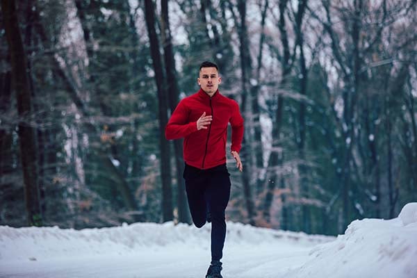 Man in a red jacket running on a snowy road through a winter forest