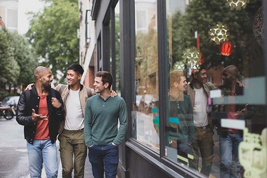 Three young men laughing together as they walk down a city sidewalk