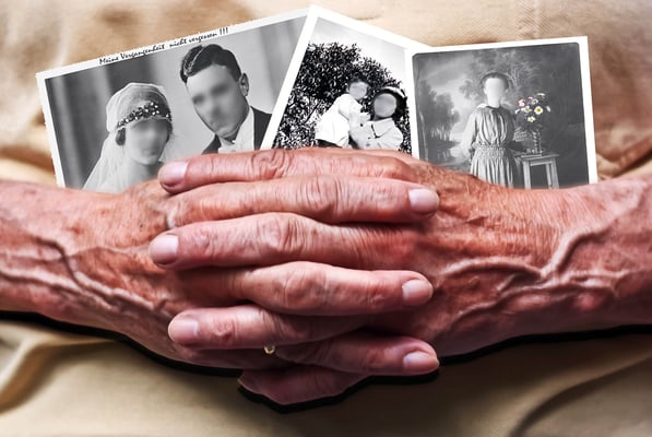 Older person's wrinkled hands clasped over old black-and-white family photos