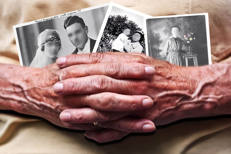 Older person's wrinkled hands clasped over old black-and-white family photos
