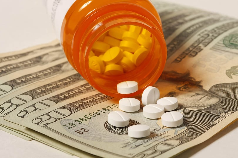 Pill bottle tipped over with tablets spilling onto twenty-dollar bills