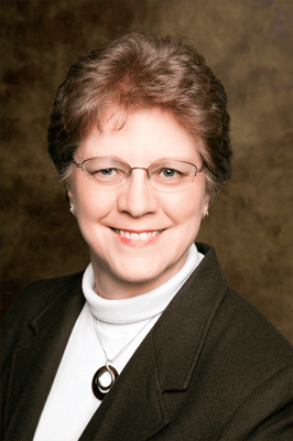 Dr. Alieta Eck smiling in glasses, a white turtleneck and a dark blazer