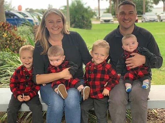 Chris Goettig and his wife on a bench with their four young sons, two sets of twins, in matching plaid shirts