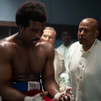 Scene from the film Big George Foreman: a boxer with wrapped hands in a locker room as an older man looks on