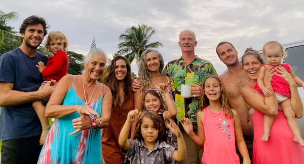 Janet E. with her husband and extended family, adults and young children smiling together under palm trees