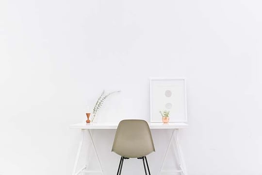 Minimalist white room with a simple desk, a gray chair, a framed print and a small plant