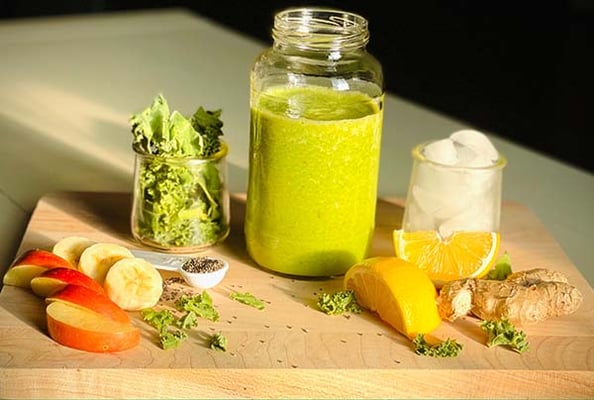 Green smoothie in a jar on a cutting board with kale, apple, banana, lemon, ginger, chia seeds and ice