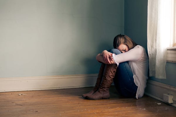 Young woman sitting in the corner of an empty room, hugging her knees with her head down