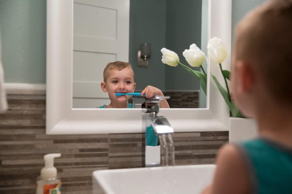 Young boy brushing his teeth, reflected in a bathroom mirror above a running faucet