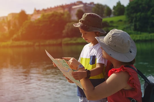 Woman in a sun hat holding a map as a young boy in a bucket hat points to it beside a river