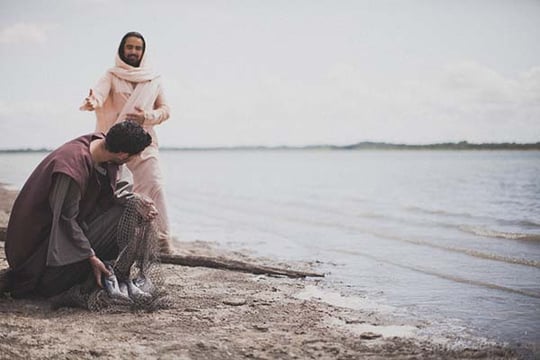 Biblical-era scene of a smiling robed man reaching toward a fisherman kneeling with his net on a lakeshore