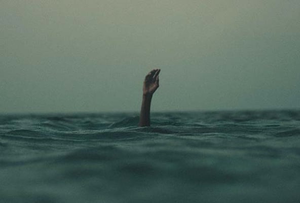 Hand reaching up out of dark, choppy water under an overcast sky