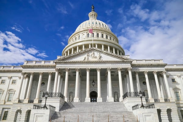 U.S. Capitol building under a blue sky, with the American flag flying above the entrance