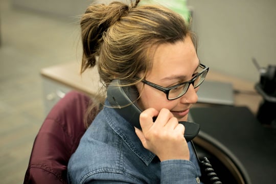 Smiling woman in glasses talking on a desk phone in an office