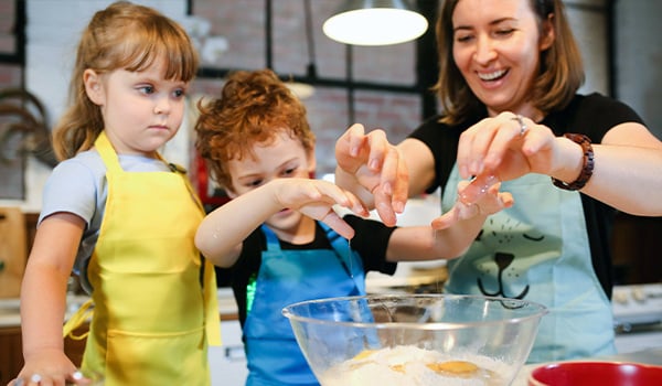 Woman and two young children in aprons mixing eggs and flour in a glass bowl in a kitchen